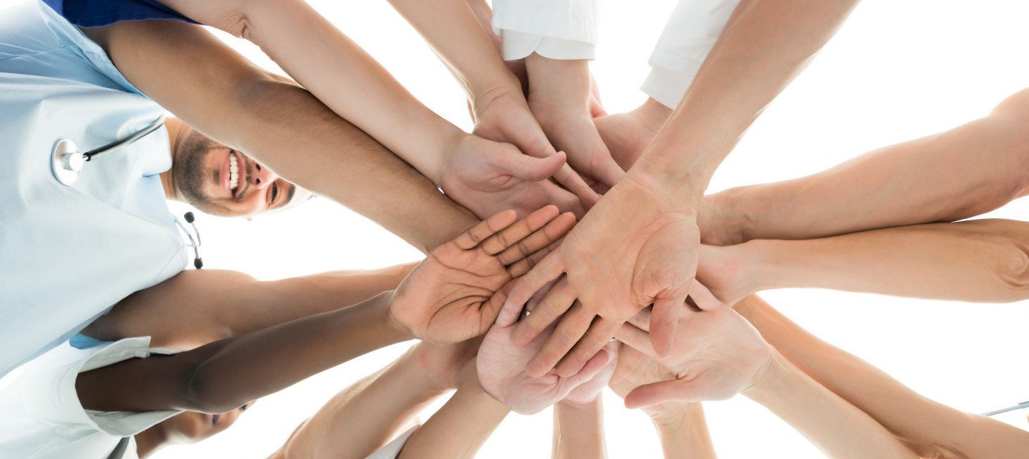 Mehrere Aerzte im Kreis mit Hände in der Mitte